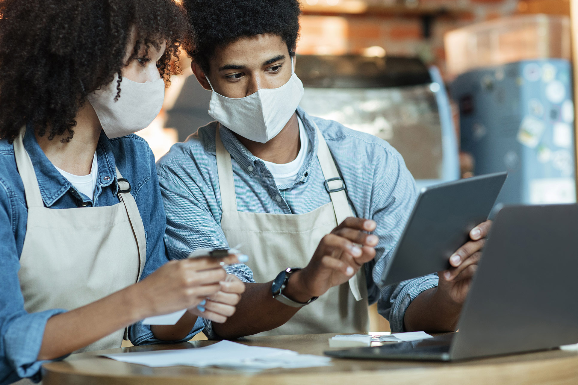 Two masked restaurant employees with white aprons in front of a computer